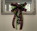Large bow comprised of 2.5" Black, orange, purple and lime plaid ribbon, 7/8" lime with black polka dot satin ribbon, and a 7/8" black satin ribbon hanging from the bottom of a mirror.