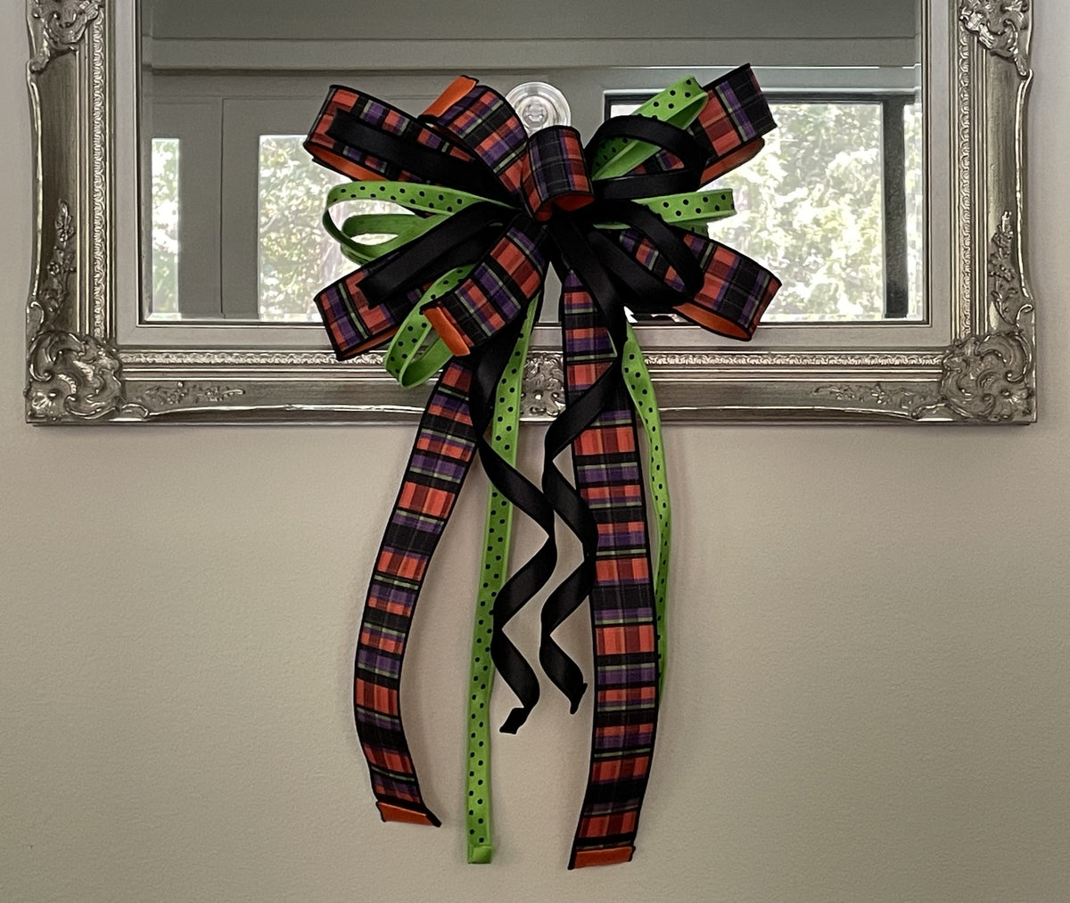 Large bow comprised of 2.5" Black, orange, purple and lime plaid ribbon, 7/8" lime with black polka dot satin ribbon, and a 7/8" black satin ribbon hanging from the bottom of a mirror.