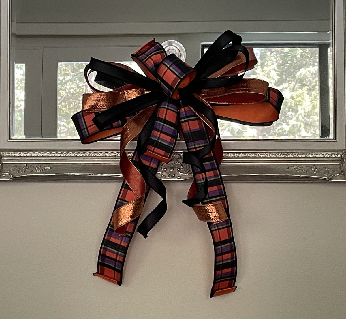 Halloween bow comprised of 2.5" black, orange, purple, and lime ribbon with an orange sating backing, 1.5" Metallic Copper Lame Ribbon, and 7/8" black satin hung from the bottom of a mirror.