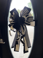 Extra large bow comprised for 5 different black and white ribbons hanging in the center of a wooden door with an oval glass panel.