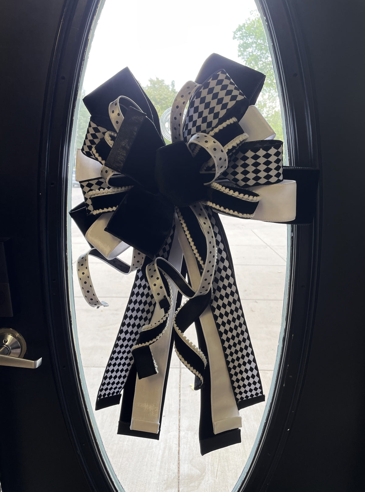 Extra large bow comprised for 5 different black and white ribbons hanging in the center of a wooden door with an oval glass panel.