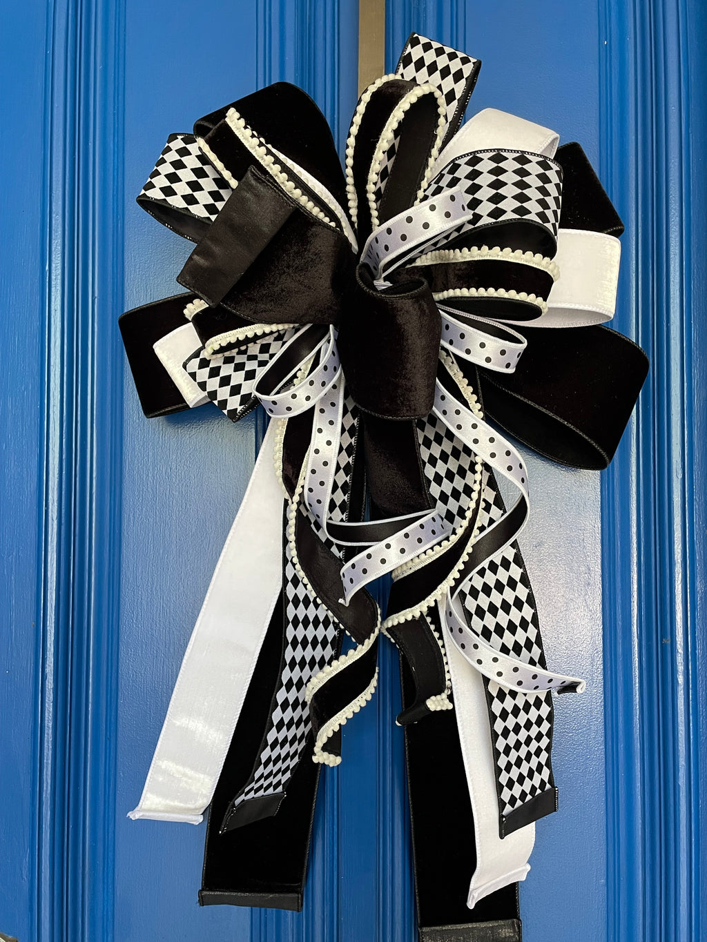 Extra large bow comprised for 5 different black and white ribbons hanging on a blue background.