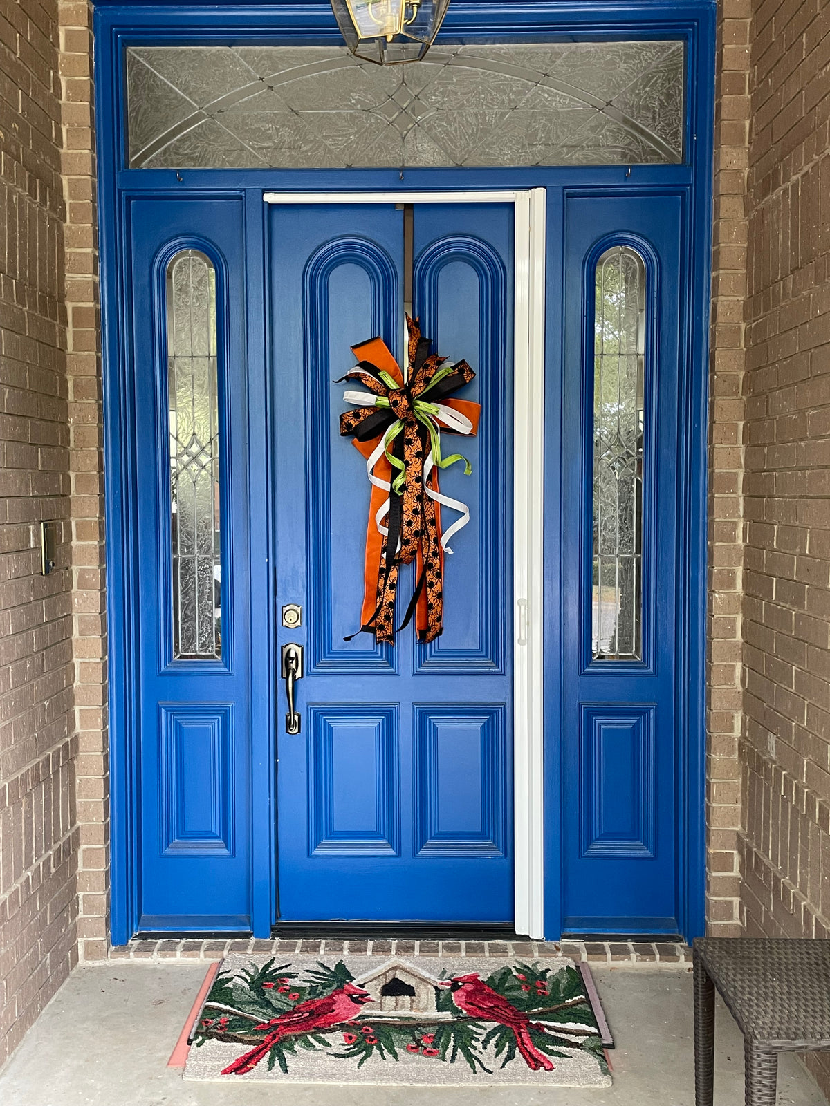 Wide angle view of a bow comprised of 4" Orange w/ black backing double-fused dupion ribbon 2.5"Orange w/ black flocked spiders and flocked black backing ribbon 1.5" d. stevens Black pleated metallic ribbon 1" White pleated metallic ribbon 1" Lime green ribbon with lime rhinestone center hanging from a blue door