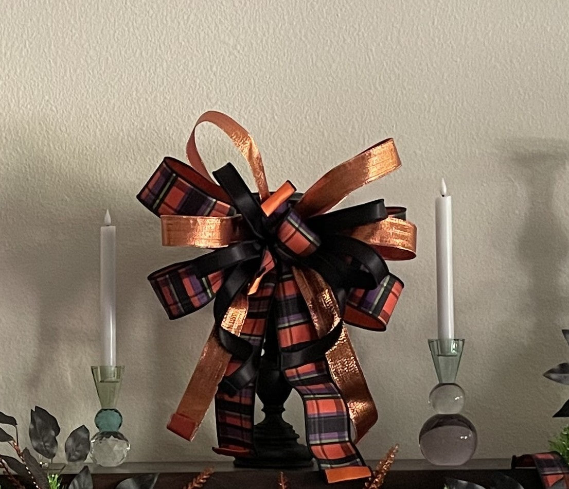 Halloween bow comprised of 2.5" black, orange, purple, and lime ribbon with an orange sating backing, 1.5" Metallic Copper Lame Ribbon, and 7/8" black satin hung from the bottom of a mirror.