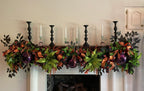 A festive autumn fireplace mantel decorated with a green garland featuring orange and black plaid accents, purple ornaments, larger glittery lime green poinsettias, and black candlesticks against a beige wall.