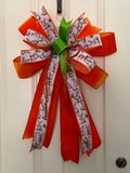Large decorative bow for wreaths or door hangers comprised of a 4" Farrisilk orange velvet ribbon, a 2.5" Easter bunny ribbon, and a 1/2" d stevens orange jeweled rope on a neutral background