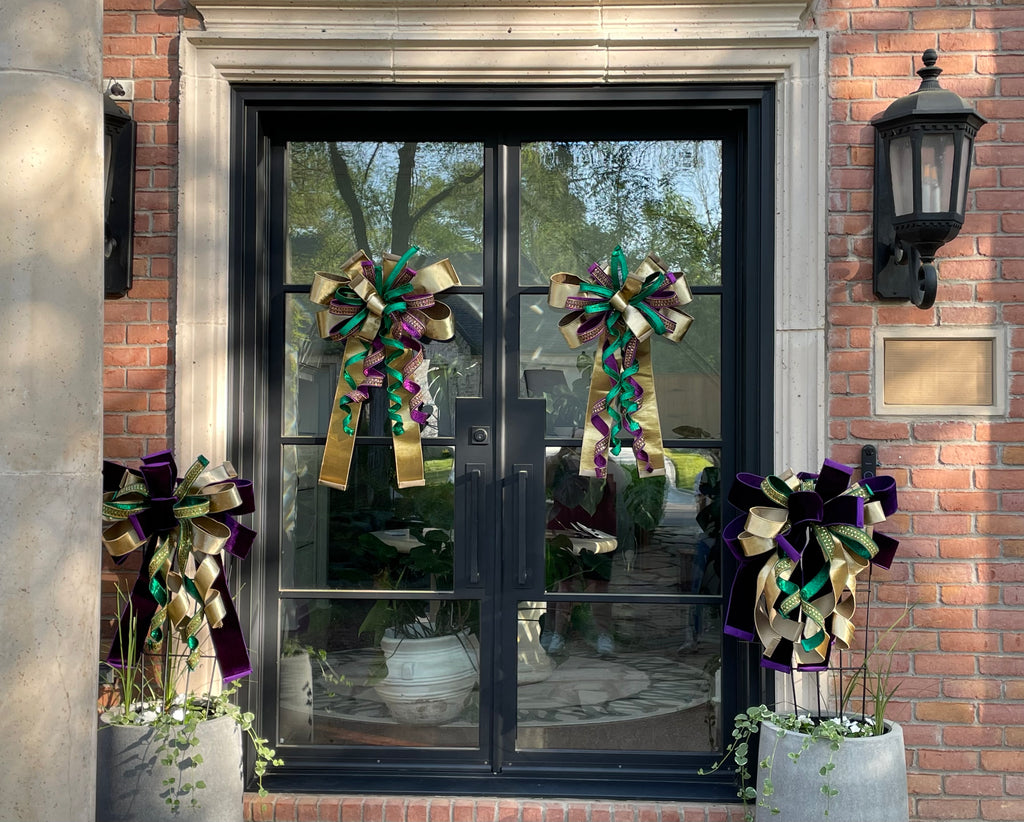 2 pairs of matching decorative bows with 1 pair hung from glass front doors and the other pair hung from a trellis in large grey planters