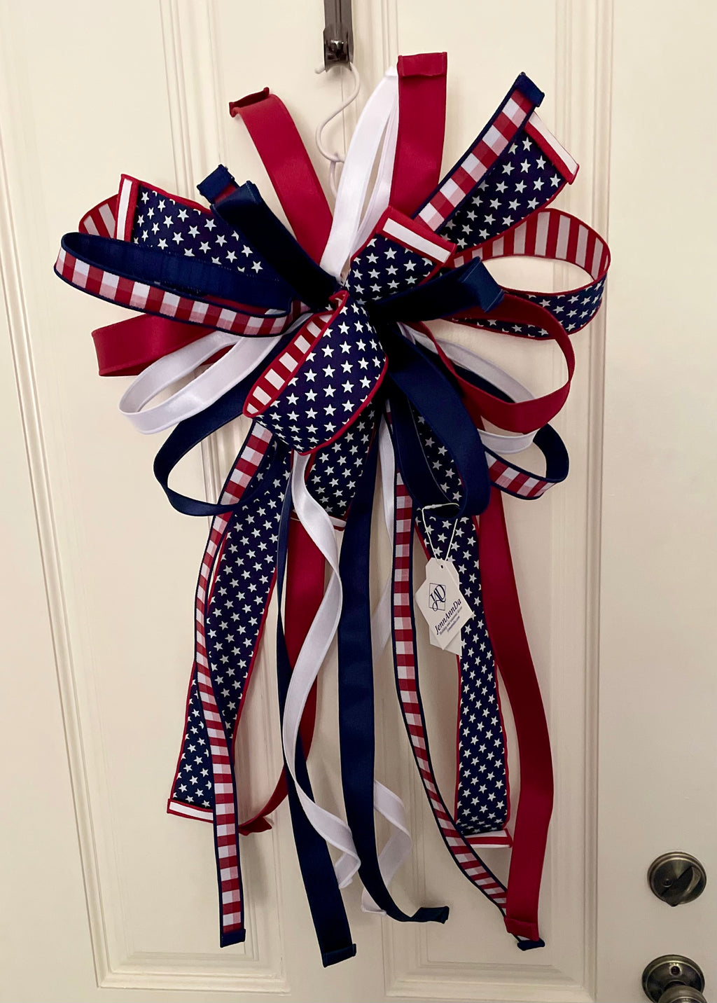 Large decorative bow for wreaths or door hangers comprised of a 1" d. stevens red and white check ribbon with navy blue dupion backing, a 2.5" stars and stripes ribbon, a 1.5" red satin ribbon, a 1.5" navy satin ribbon, and a 1" white satin ribbon on a neutral background. Shown with tails uncurled.