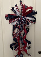 Large decorative bow for wreaths or door hangers comprised of a 1" d. stevens red and white check ribbon with navy blue dupion backing, a 2.5" stars and stripes ribbon, a 1.5" red satin ribbon, a 1.5" navy satin ribbon, and a 1" white satin ribbon on a neutral background. Shown with tails curled.