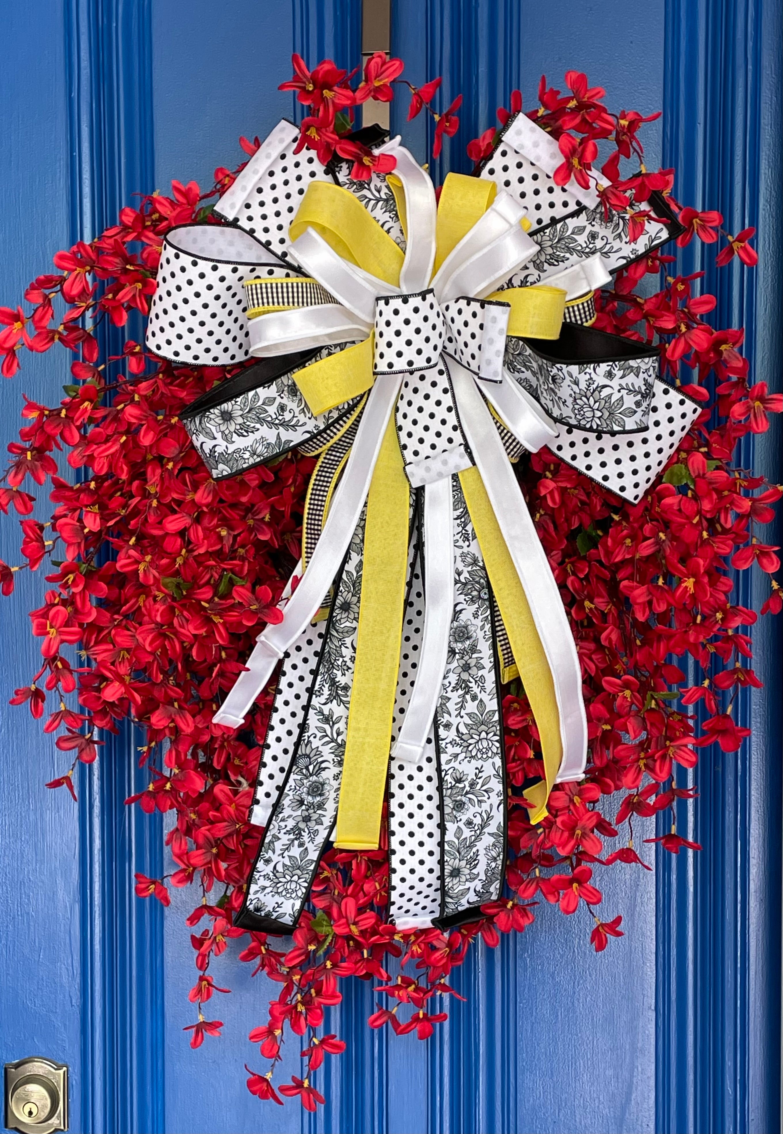 Closeup view of a decorative wreath with dainty red flowers and a bow comprised of a 4" Farrisilk White w/ Black Polka Dots ribbon, a 2.5" Black and white chinoiserie ribbon, and a 1" white satin ribbon on a neutral colored door.