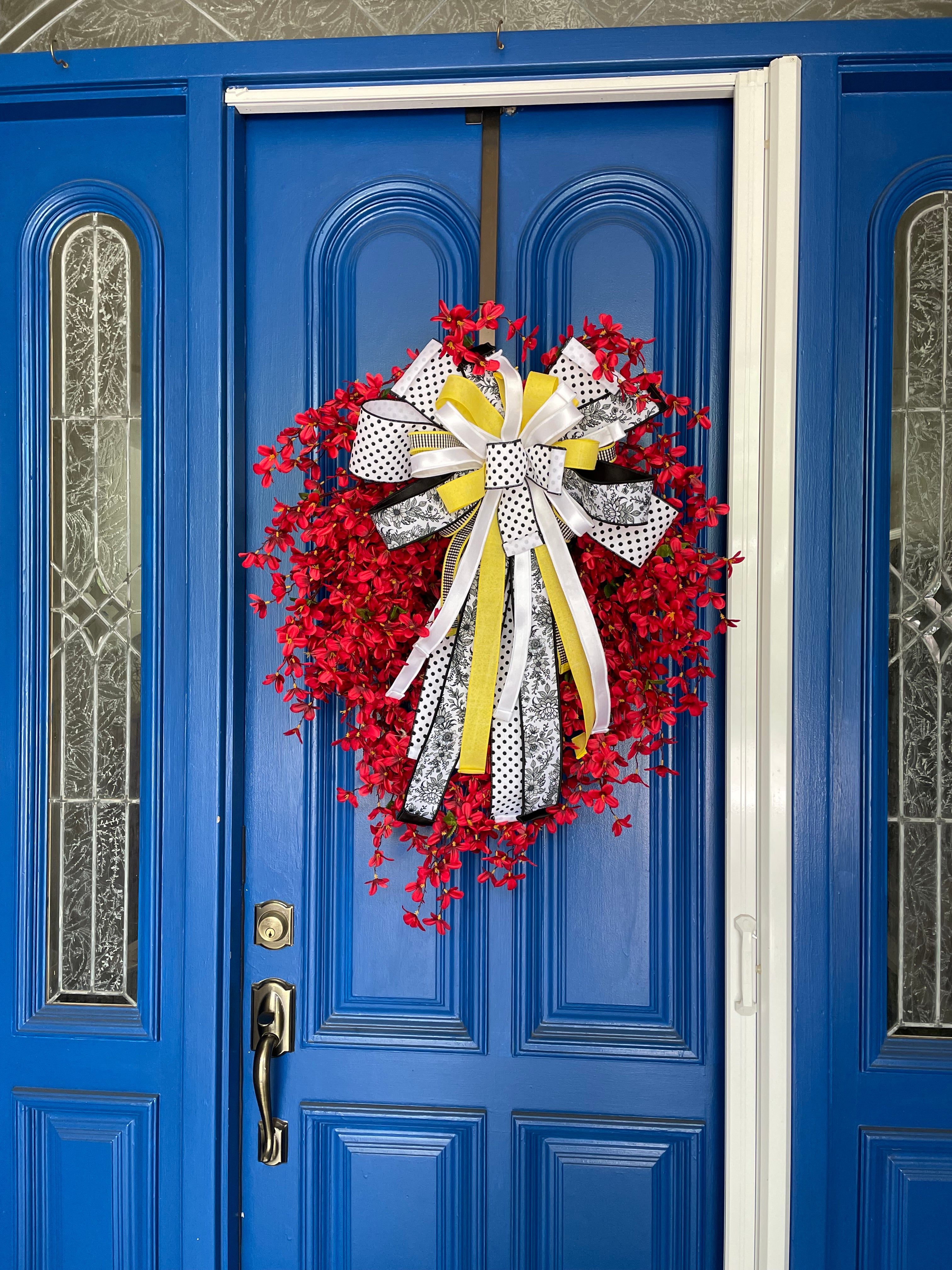 Wide view of a decorative wreath with dainty red flowers and a bow comprised of a 4" Farrisilk White w/ Black Polka Dots ribbon, a 2.5" Black and white chinoiserie ribbon, and a 1" white satin ribbon on a neutral colored door.