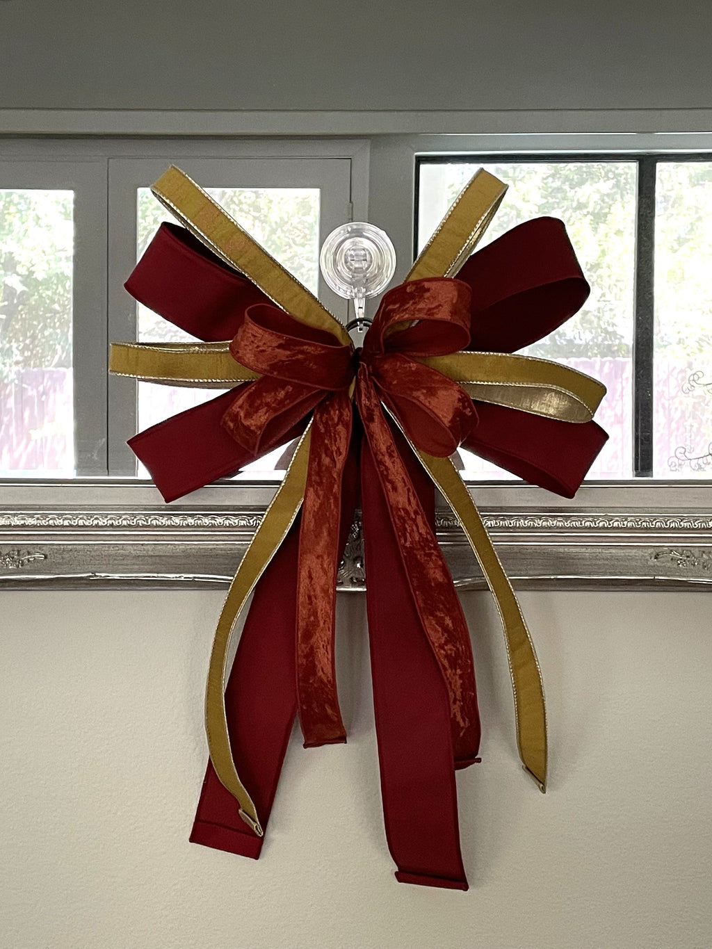 Designer bow compromised of 2/5" Burgundy taffeta ribbon, 1" gold dupion ribbon, and 1.5" dark orange ribbon mounted on a mirror.