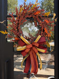 Designer bow compromised of 2/5" Burgundy taffeta ribbon, 1" gold dupion ribbon, and 1.5" dark orange ribbon attached at the bottom of a fall berry wreath which is mounted on a glass door.