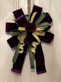Large decorative bow for wreaths or door hangers comprised of a Farrisilk 4" purple velvet ribbon, a Farrisilk 1" heavily rhinestoned green metallic ribbon, and a Farrisilk 1" pleated metallic gold ribbon on a neutral background