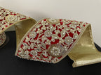 A video of close up view of a roll of 4" red ribbon with a heavily embellished, ornate floral pattern comprised of gold thread, pearls, sequins, and rhinestones and a metallic gold backing.