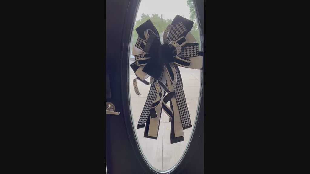 Video of an extra large bow comprised for 5 different black and white ribbons hanging in the center of a wooden door with an oval glass panel.