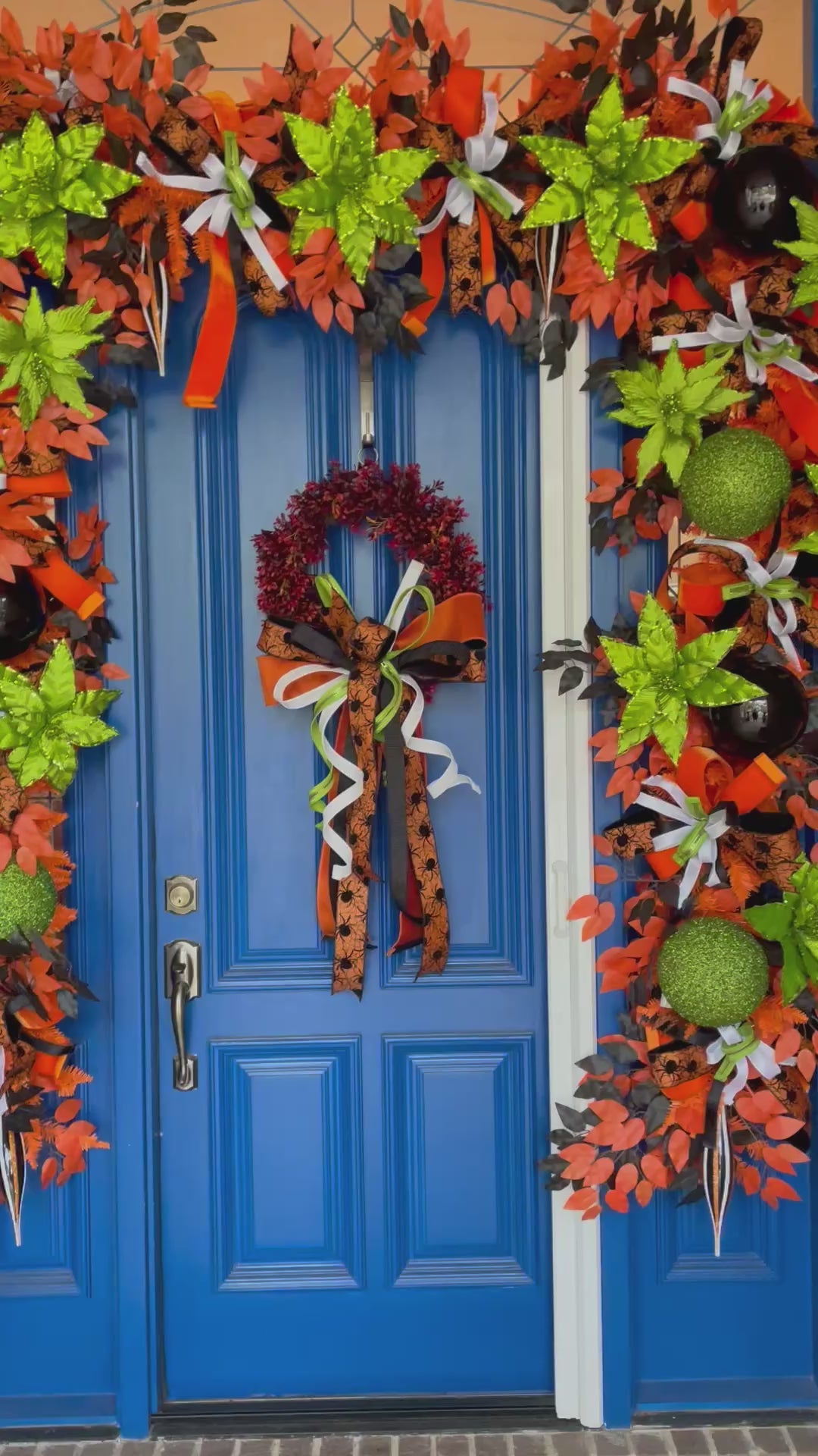 A 2nd video of an oversized blue door with a very large garland wrapped around the top and sides. There is also a wreath with a large bow. Colors include orange, black, white, and lime green.